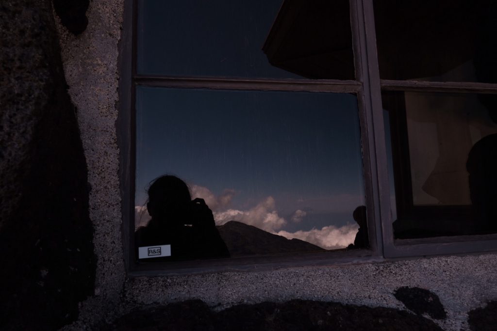 Artistic self portrait shot through the reflection of a window. The camera covers the artists face as you see the brilliant sky and clouds behind her.